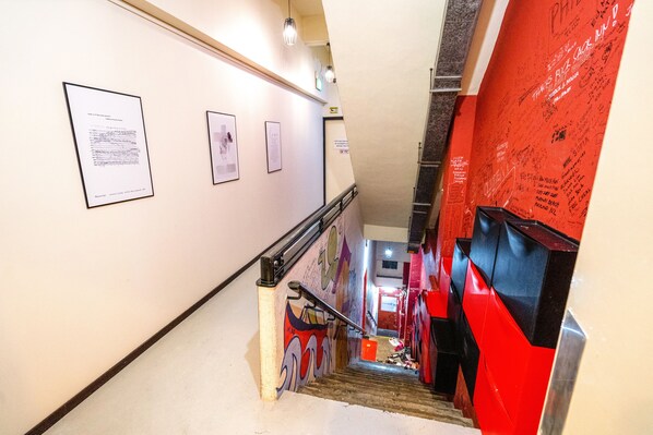 A staircase with a handrail, a red wall with graffiti, and framed documents on the wall. - Beds & Dreams Inn @ Clarke Quay (Singapore)