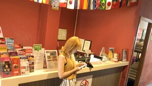 Un comptoir d’accueil avec une enseigne indiquant « Beds & Dreams » et une variété de brochures d’information. Des drapeaux sont disposés au-dessus du comptoir, et un écran d’ordinateur est visible sur le plan de travail.