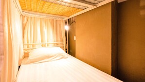 A single bed with a headboard, a window with curtains, and a light fixture on the wall. - Beds & Dreams Inn @ Clarke Quay (Singapore)