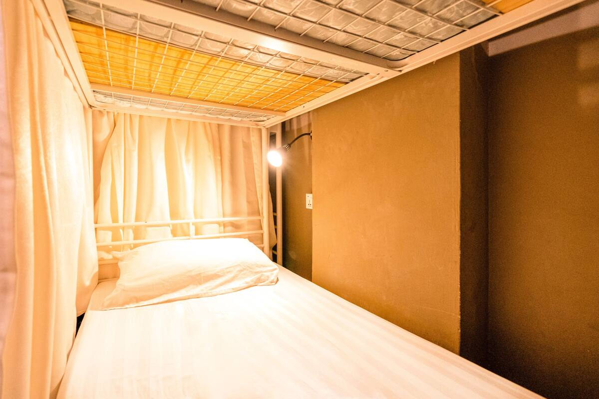 Ein Einzelbett mit Kopfteil, ein Fenster mit Vorhängen und eine Wandleuchte.