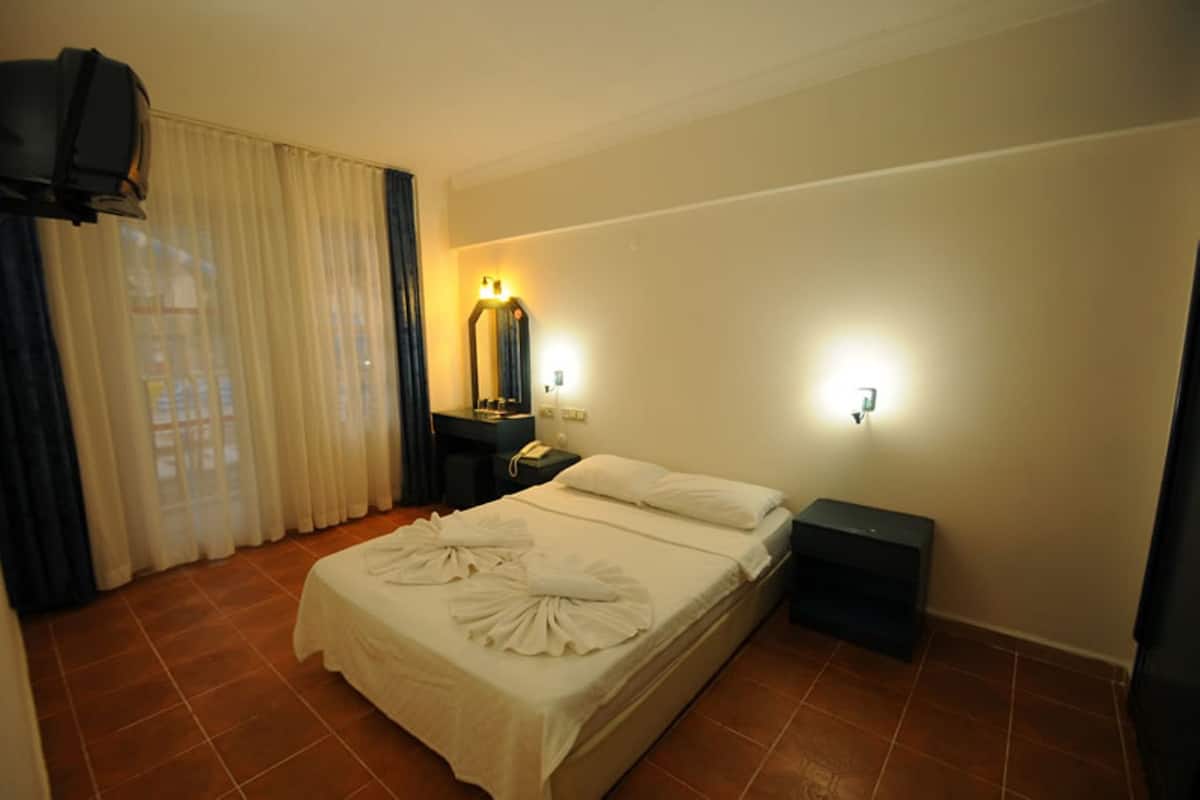 A hotel room with a bed, a nightstand, a mirror, a TV, and a window with curtains.