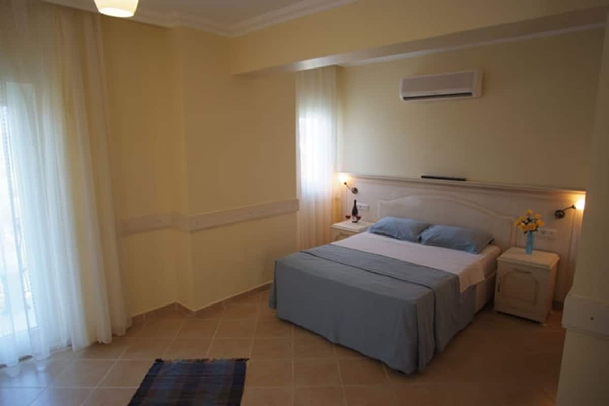 A bedroom with a bed, bedside tables, a nightstand, a lamp, and a window with curtains.
