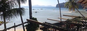 Vista de playa con palmeras y barcos en el agua.