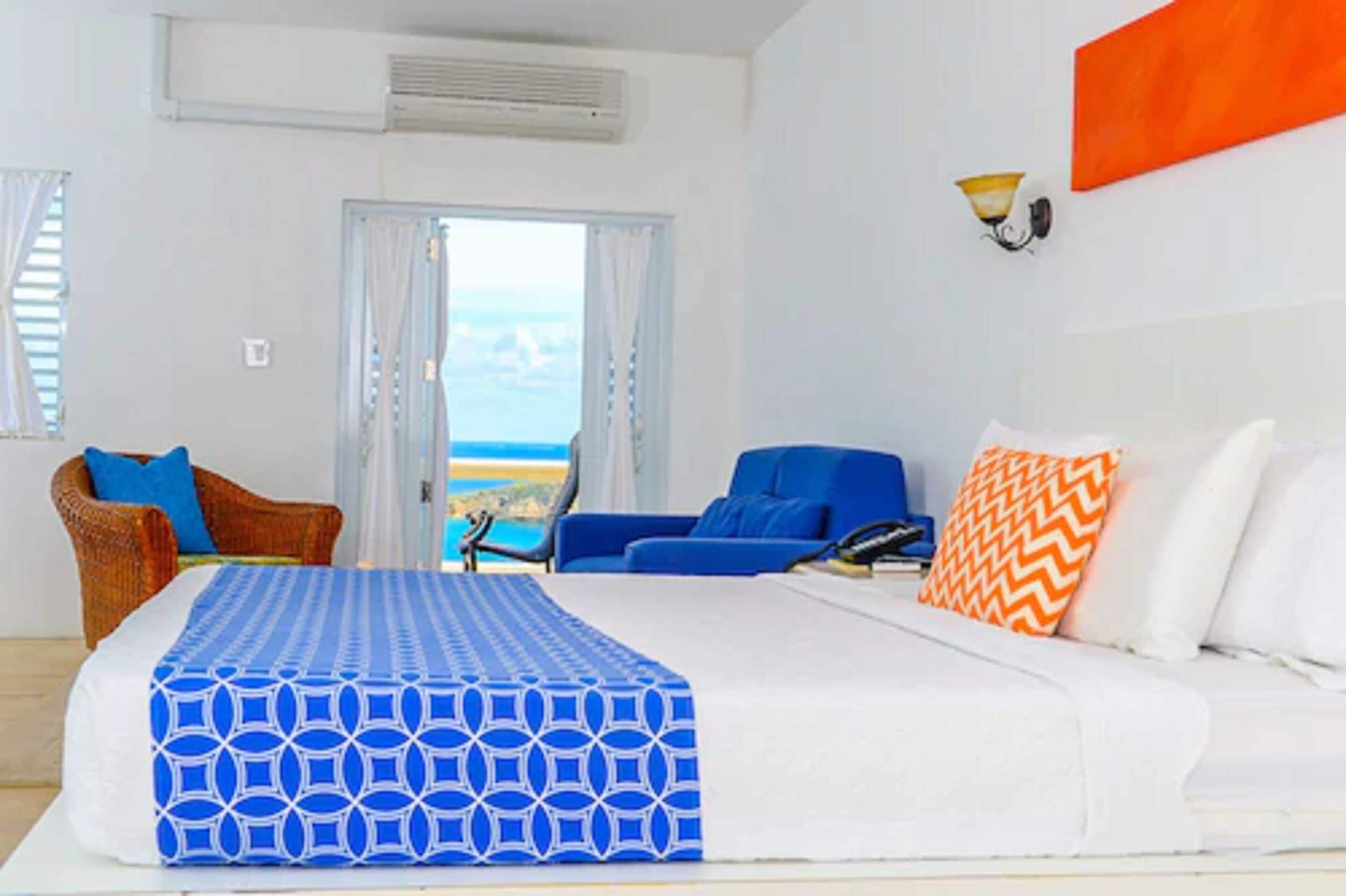 Una habitació d'hotel amb un llit, un sofà blau, un sofà blanc i vista al mar a través d'una finestra gran.