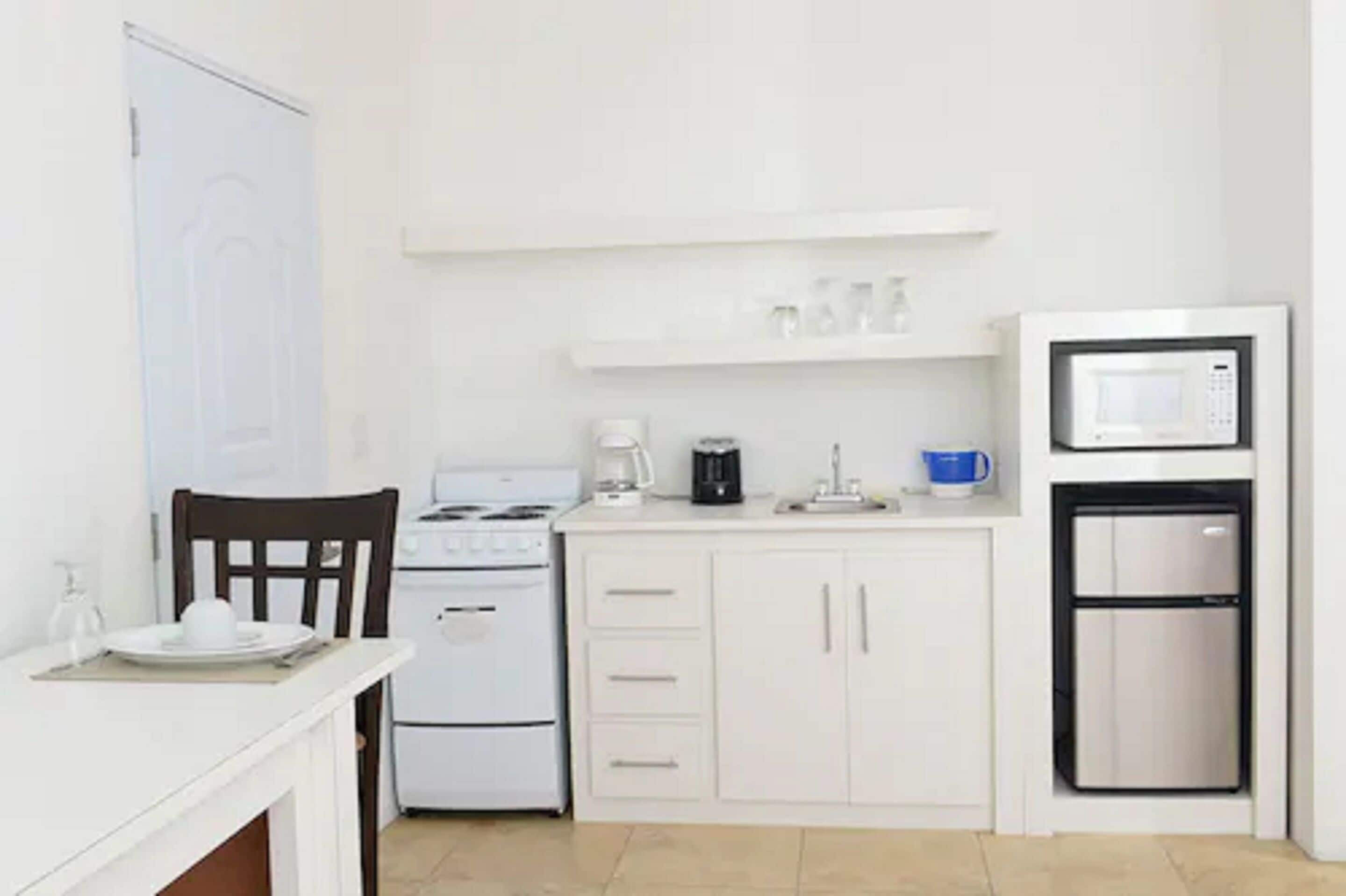 A compact kitchen with white cabinetry, a stove, a microwave, and a refrigerator.