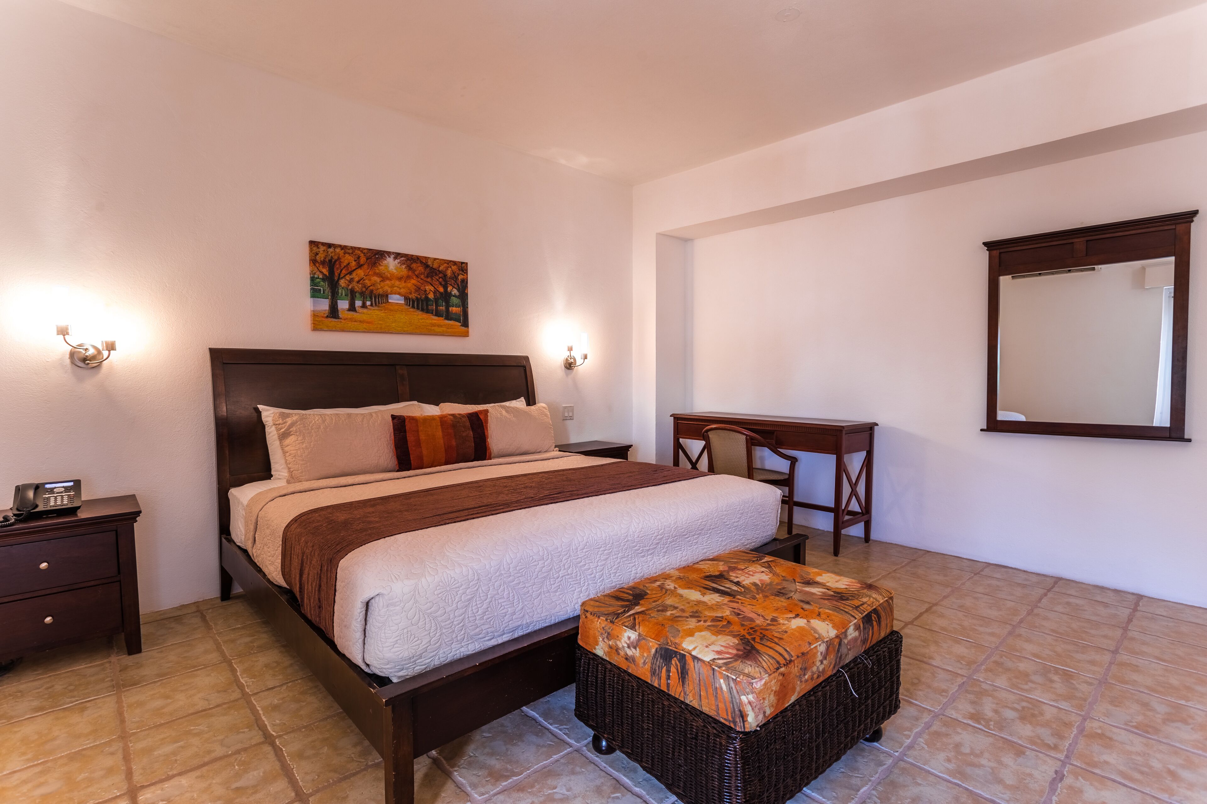 Un dormitorio con cama, mesita de noche, escritorio y un espejo grande.