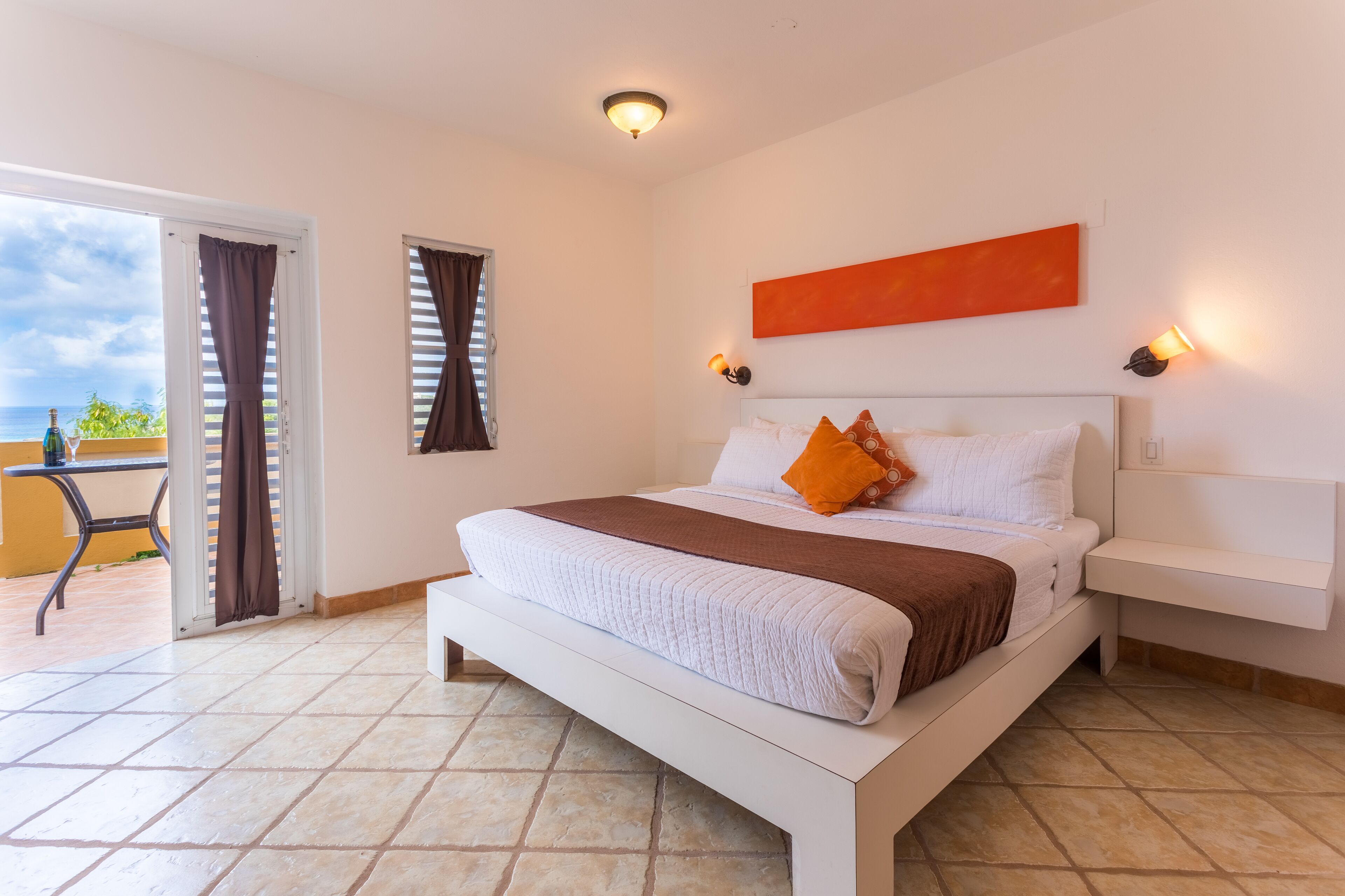 Habitación de hotel con una cama, una mesita de noche, una lámpara fijada a la pared y vistas al exterior.