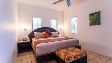 Un dormitorio con cama, mesitas de noche, ventilador de techo y lámpara de pared.