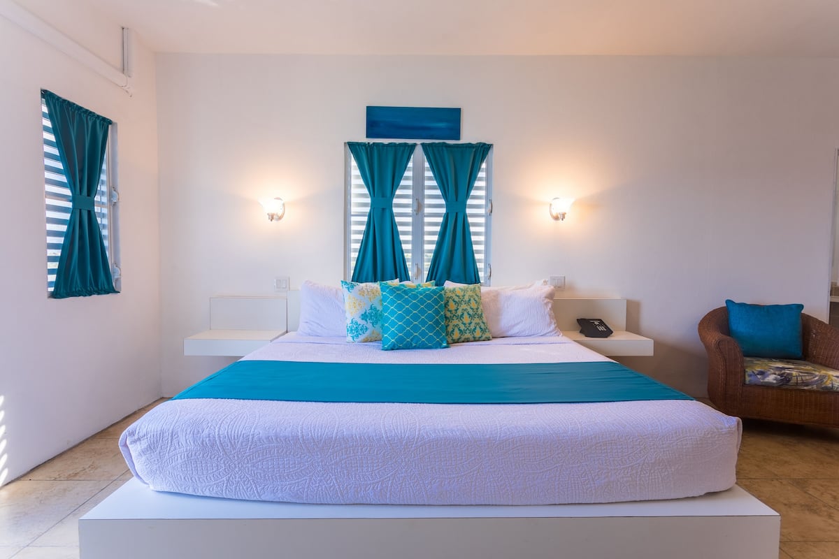 Une chambre à coucher avec un grand lit, des rideaux de couleur turquoise et une œuvre d’art bleue au-dessus de la fenêtre.