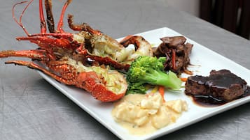 Una bandeja de mariscos con langosta, brócoli, zanahorias y un plato de carne sobre un plato blanco.