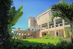 A two-story building with a flat roof, a balcony on the upper floor, and a well-maintained garden with various plants and flowers.