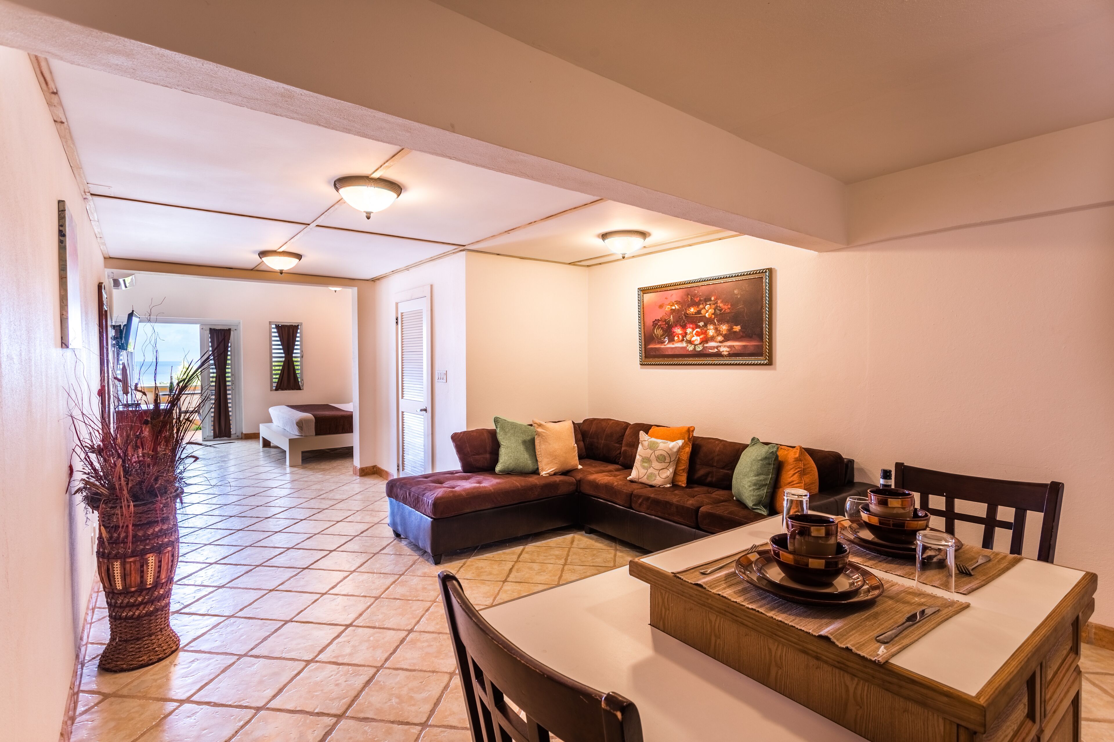 A living room with a sectional sofa, dining table, and a large vase.