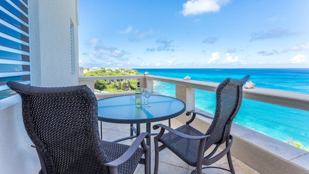 A balcony with two wicker chairs and a glass table, overlooking a turquoise sea and a clear sky. - La Vue Boutique Inn (South Hill)