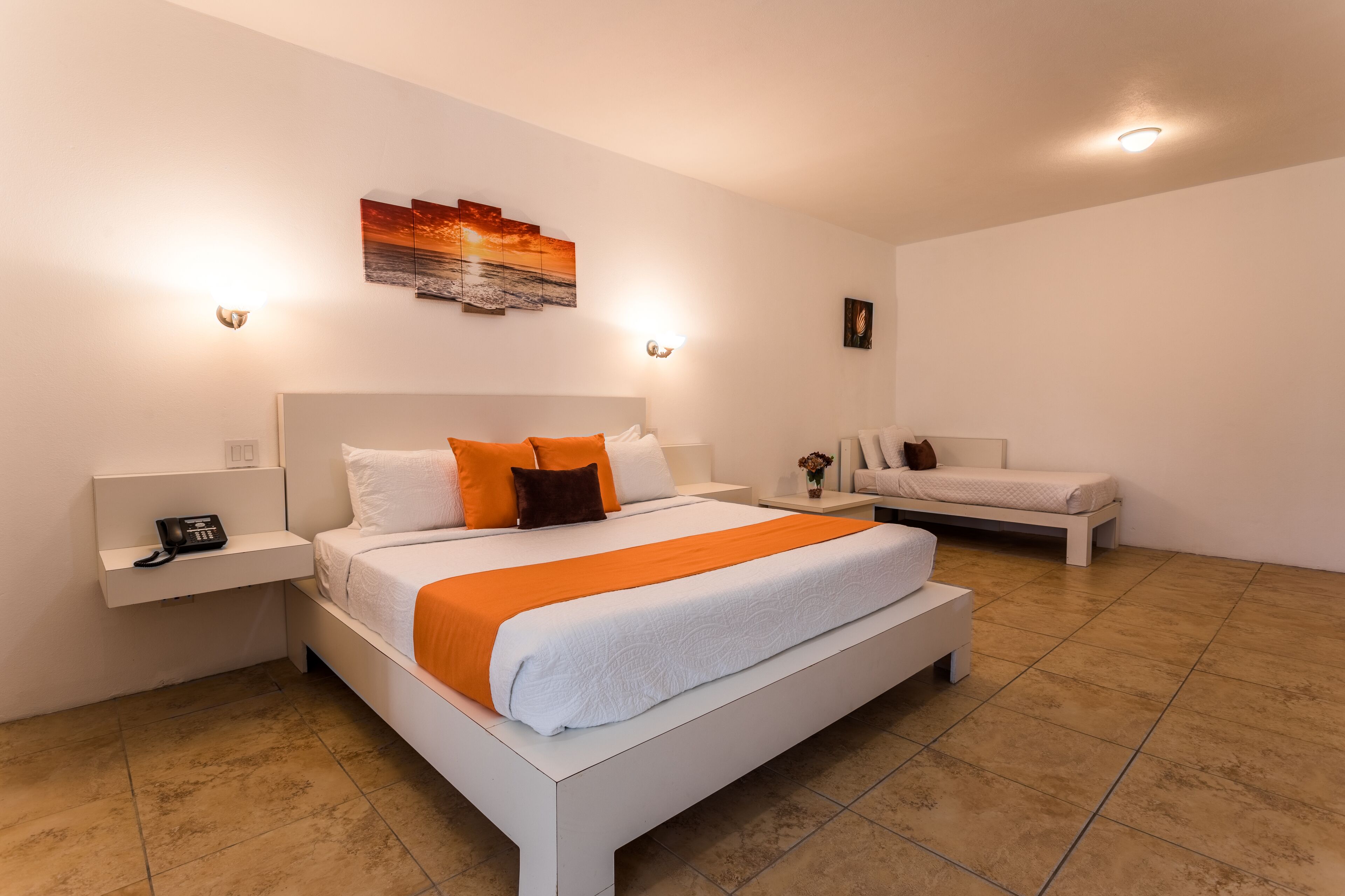 Una habitación de hotel moderna con una cama grande, una cama más pequeña, una mesita de noche con un teléfono y una obra de arte colgada en la pared.