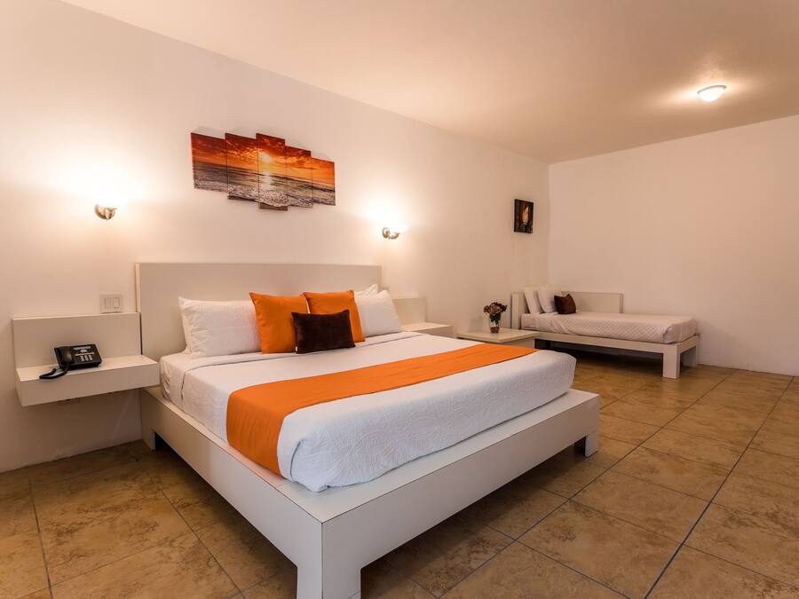 Una habitación de hotel moderna con una cama grande, una cama más pequeña, una mesita de noche con un teléfono y una obra de arte colgada en la pared.