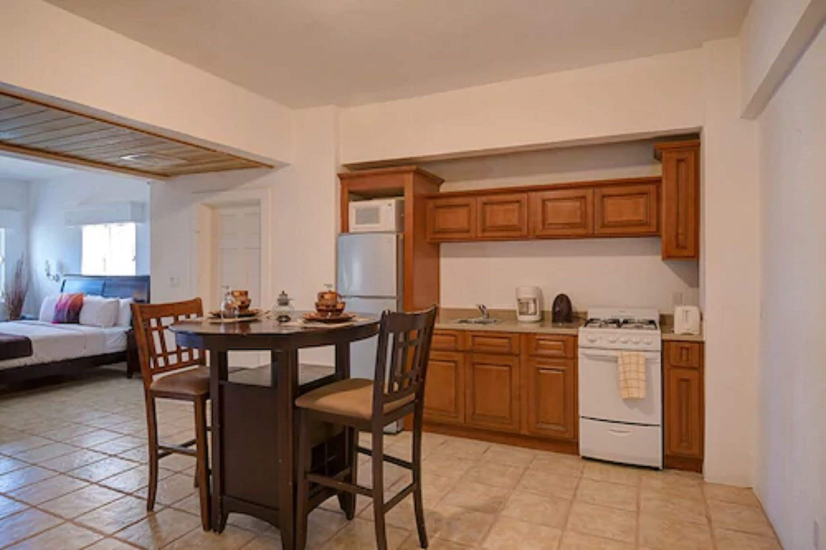 A compact kitchen with wooden cabinets, a stove, and a microwave. There is a dining table with chairs.