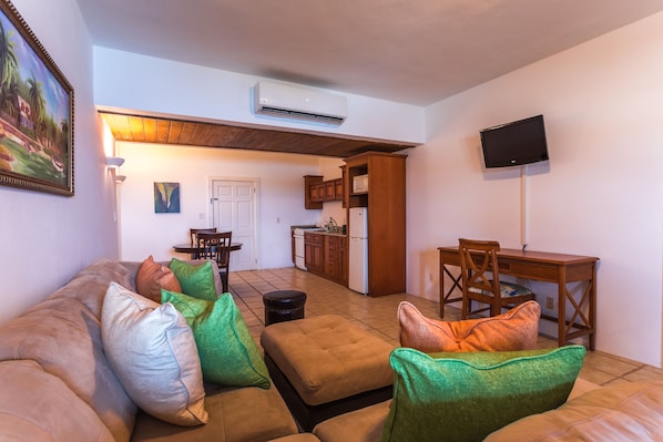 A living room with a sofa, ottoman, and chairs, a dining area with a table and chairs, a kitchen with cabinets and appliances, and a mounted TV. - La Vue Boutique Inn (South Hill)