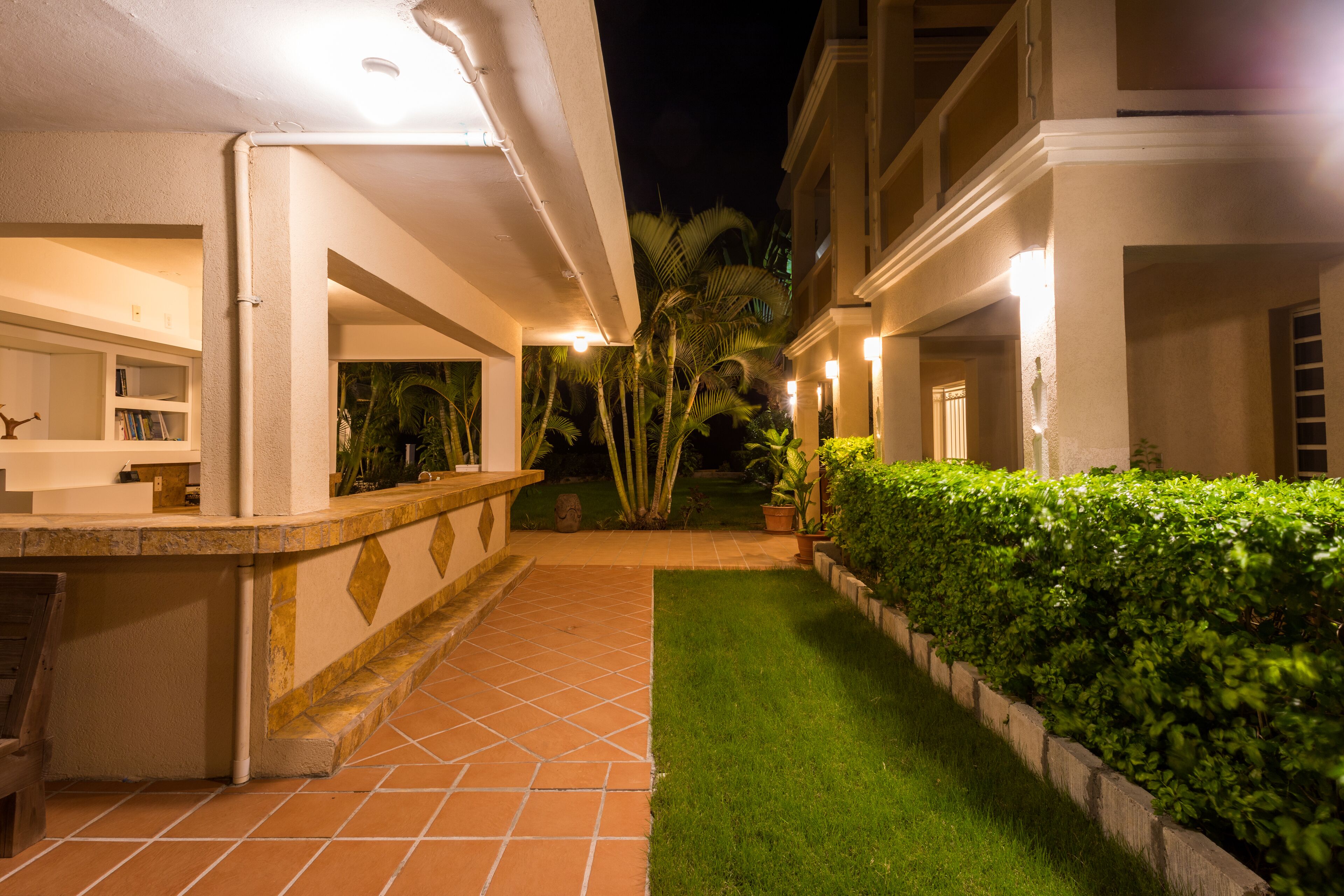 Un espace extérieur bien éclairé, avec une terrasse carrelée, une pelouse soigneusement entretenue et une haie.