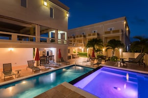 A swimming pool with lounge chairs and umbrellas, surrounded by a multi-story building with balconies.