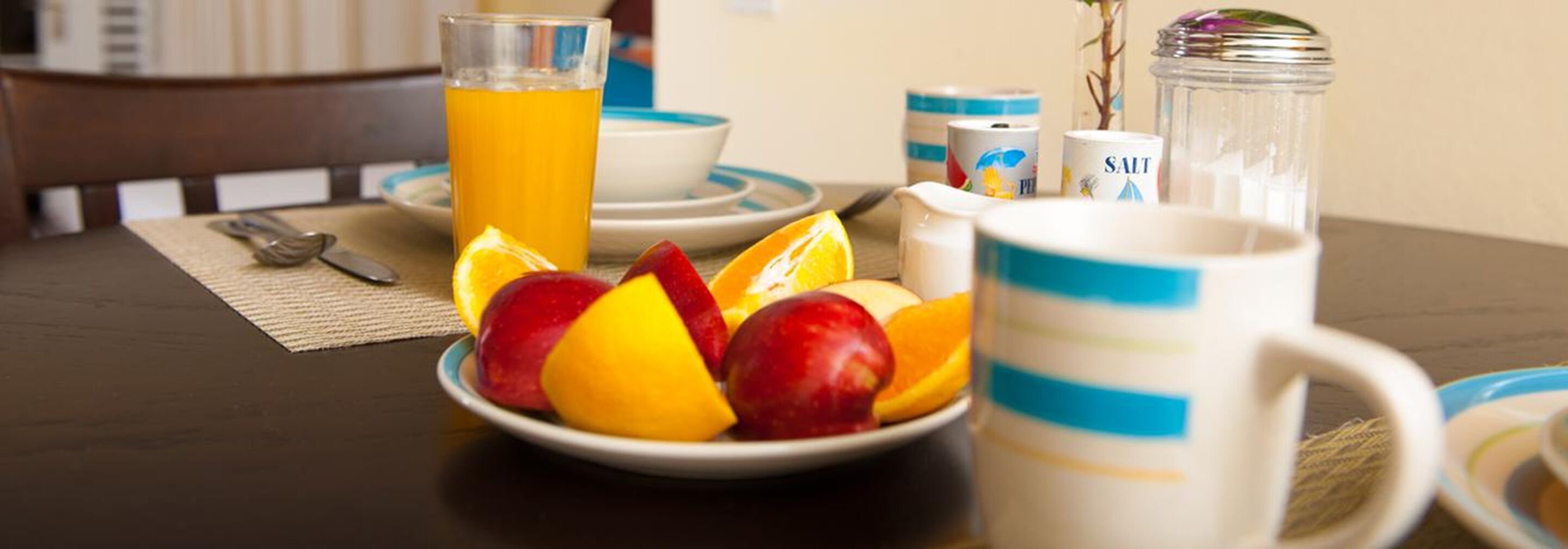 Un desayuno con un bol de fruta, un vaso de zumo de naranja y un salero sobre una mesa.