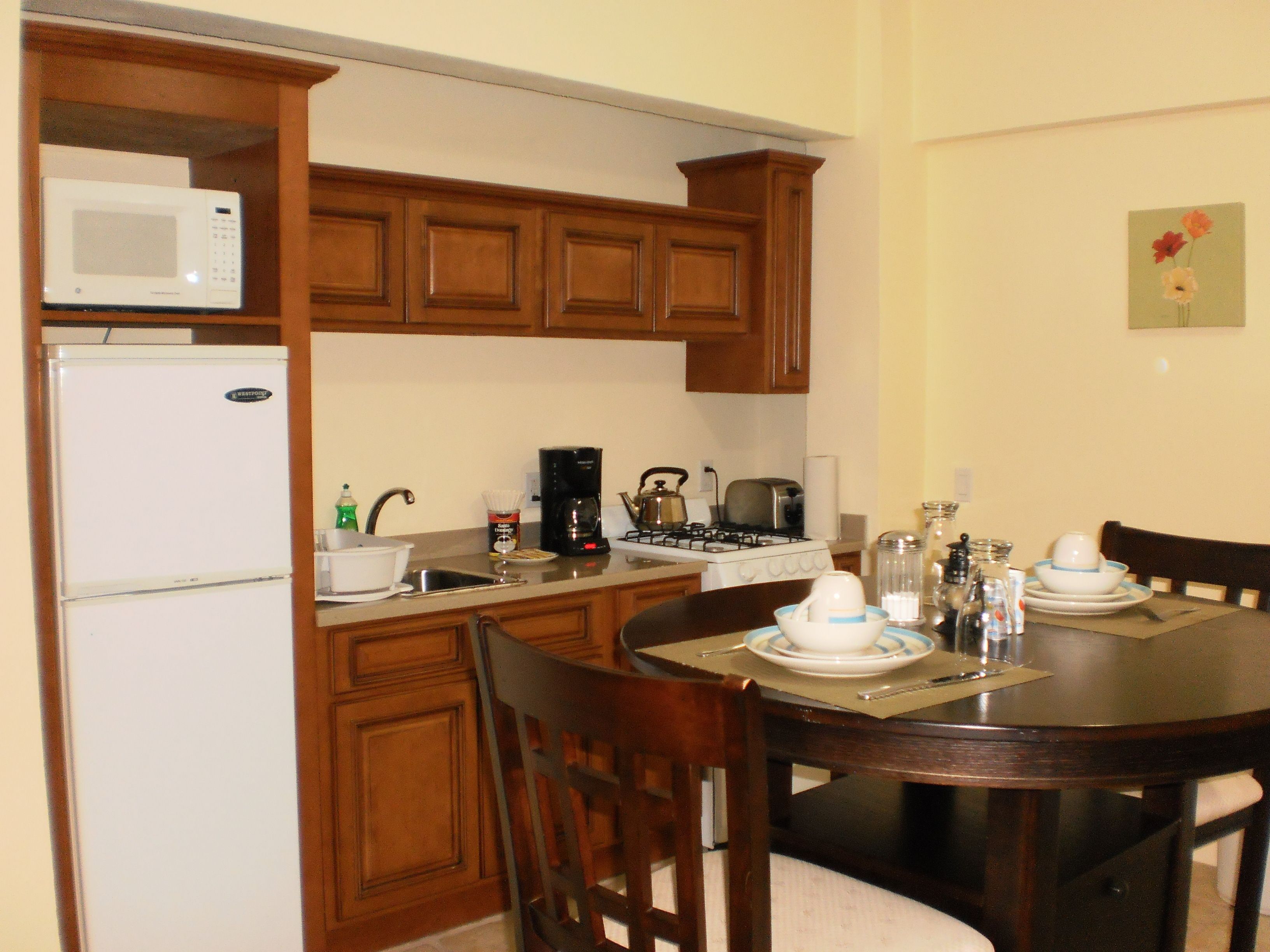 A compact kitchen with wooden cabinets, a microwave, a stove, and a dining table set for four.