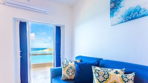 A room with a blue sofa, patterned cushions, a painting, and a view of the sea through a glass door. - La Vue Boutique Inn (South Hill)
