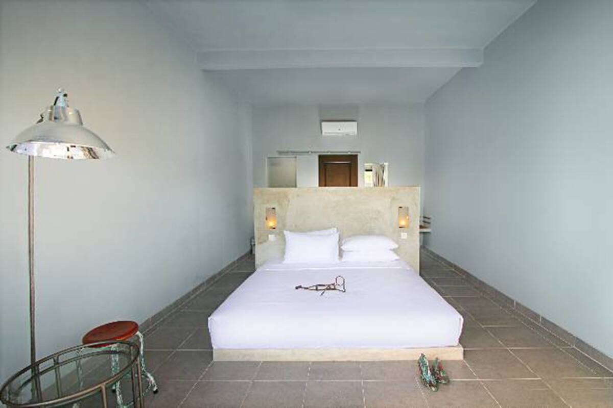 A hotel room with a large bed, a bedside table, a floor lamp, and a small stool.