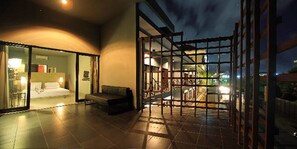 A modern hotel room with a glass door leading to a balcony, a sofa, and a bed. - The Grey Boutique Inn (Legian)