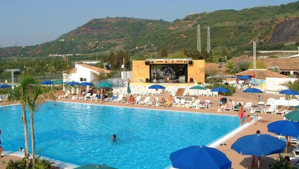 A swimming pool with lounge chairs and umbrellas, surrounded by buildings and hills. - TH Pizzo Calabro - Porto Ada Village (Pizzo)