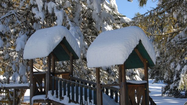 Un kiosque en bois, dont le toit est recouvert de neige, et un escalier en bois qui y mène.