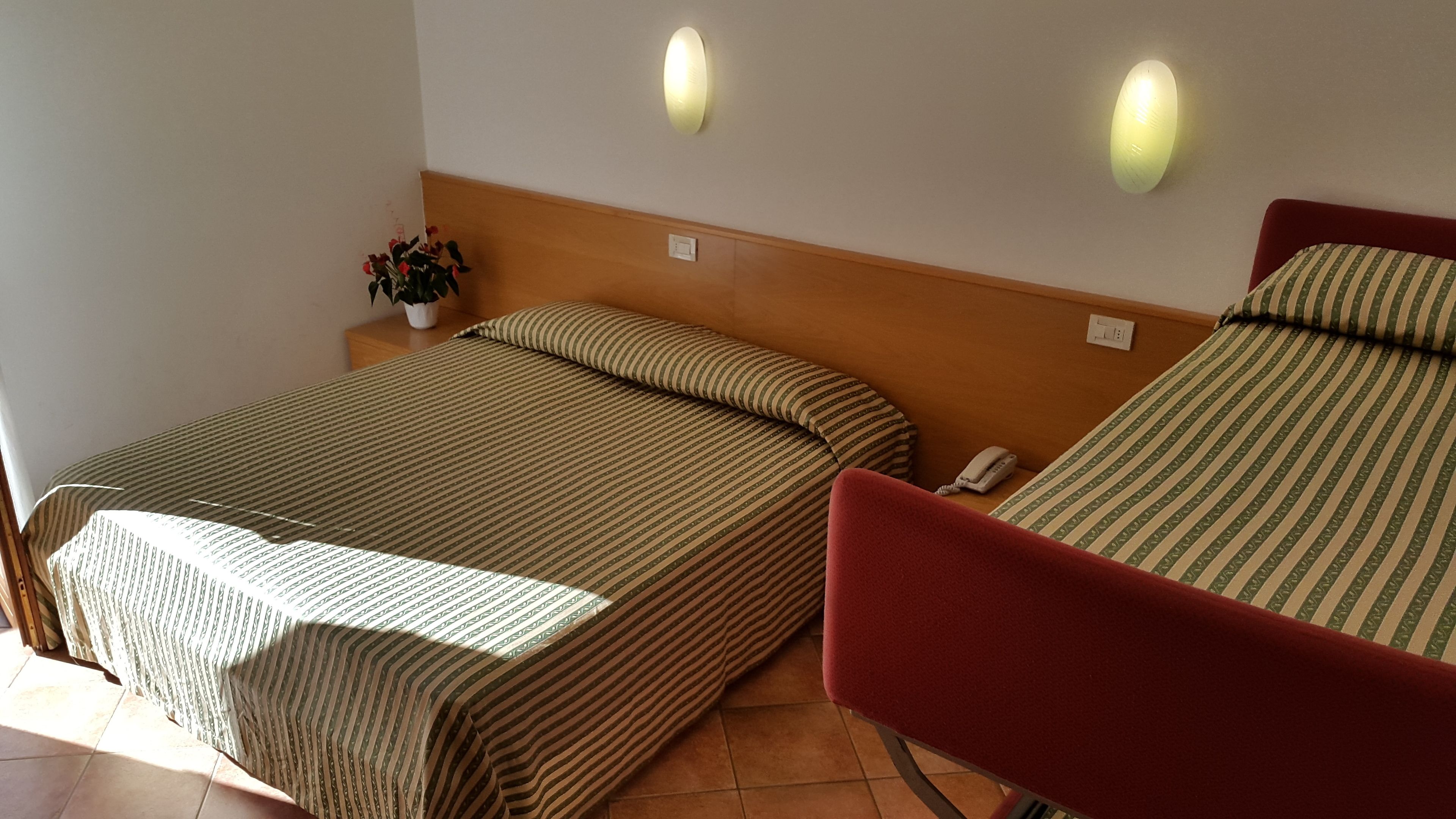 Een hotelkamer met twee bedden, een nachtkastje met een telefoon, en een wandlamp.