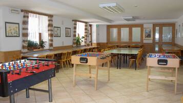 Una stanza con due tavoli da calcio, sedie di legno e un tavolo lungo.