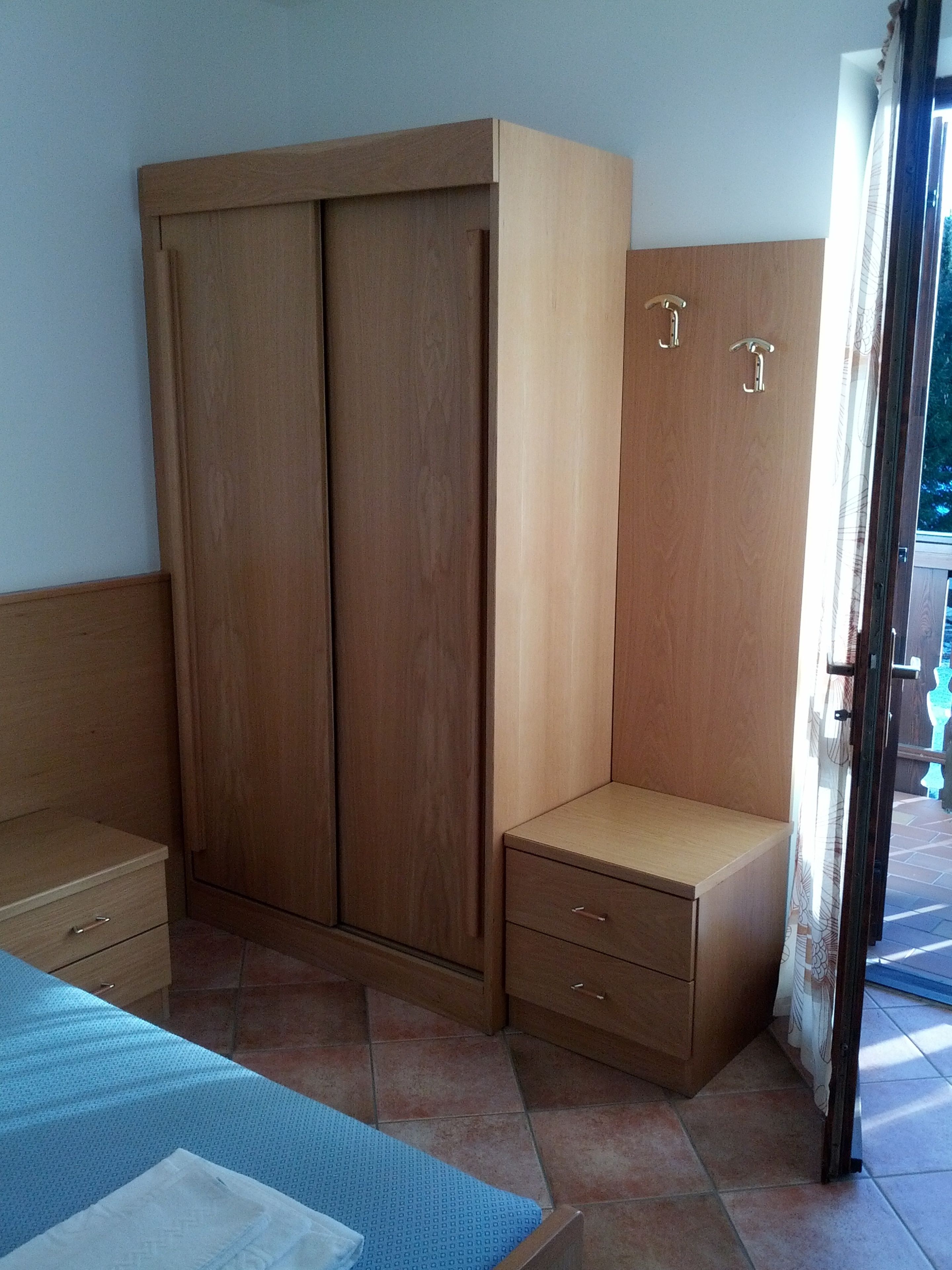 Ein Schlafzimmer mit einem Holzschrank, einem kleinen Nachttisch und einem Bett mit blauer Bettdecke.