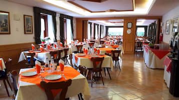 Ein Restaurant mit mehreren Tischen, jeweils mit orangefarbenen Tischdecken, weißen Tellern und klarem Glas.