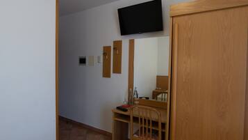 Een kamer met een houten bureau, een stoel, een aan de muur bevestigde televisie en een houten kledingkast.