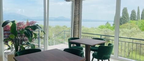 Un área de comedor con una mesa y sillas, ventanas amplias con vistas a zonas verdes y montañas, y un balcón con barandilla.