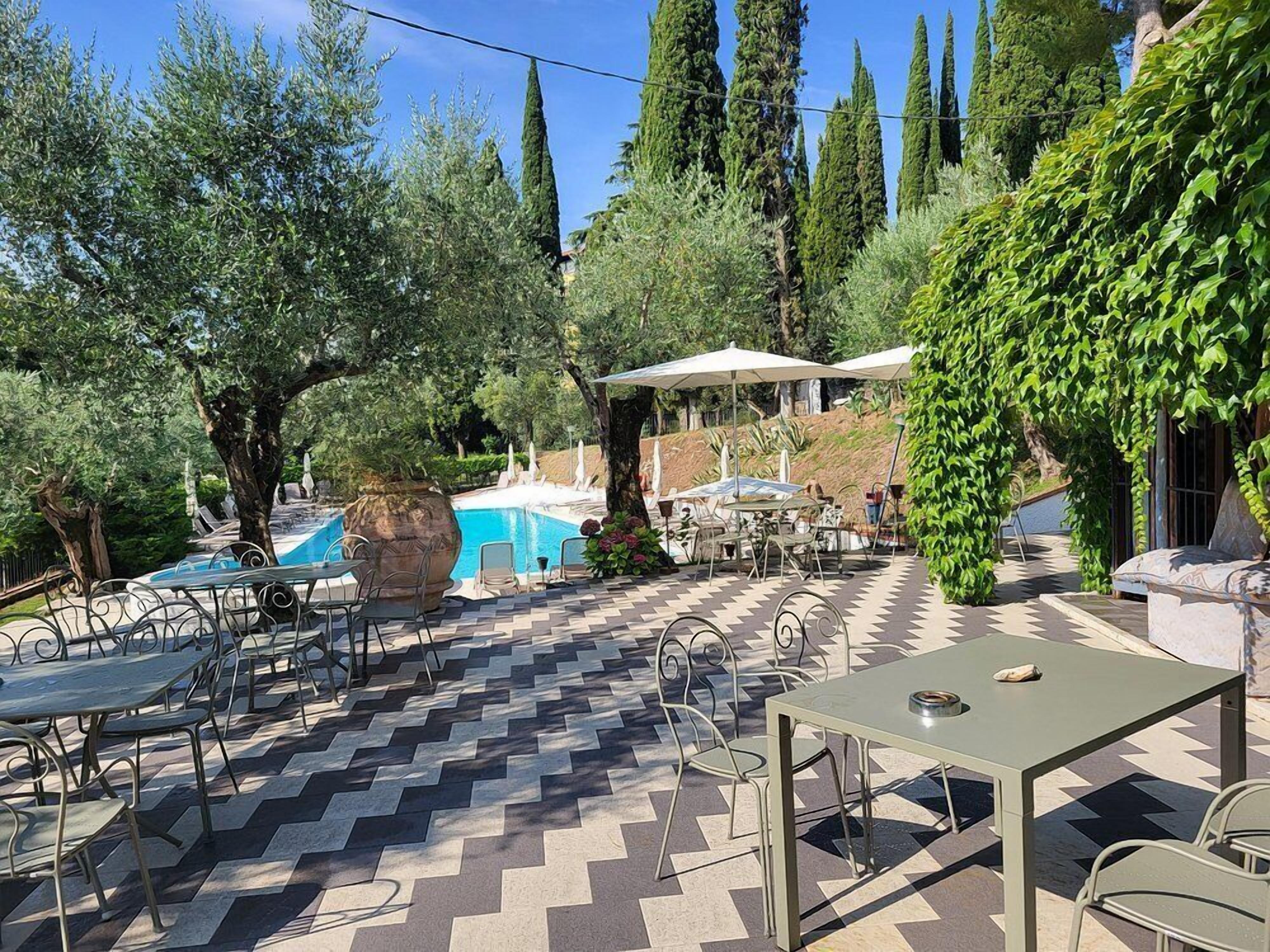 Un patio exterior con piscina, rodeado de árboles y zonas de estar cubiertas.