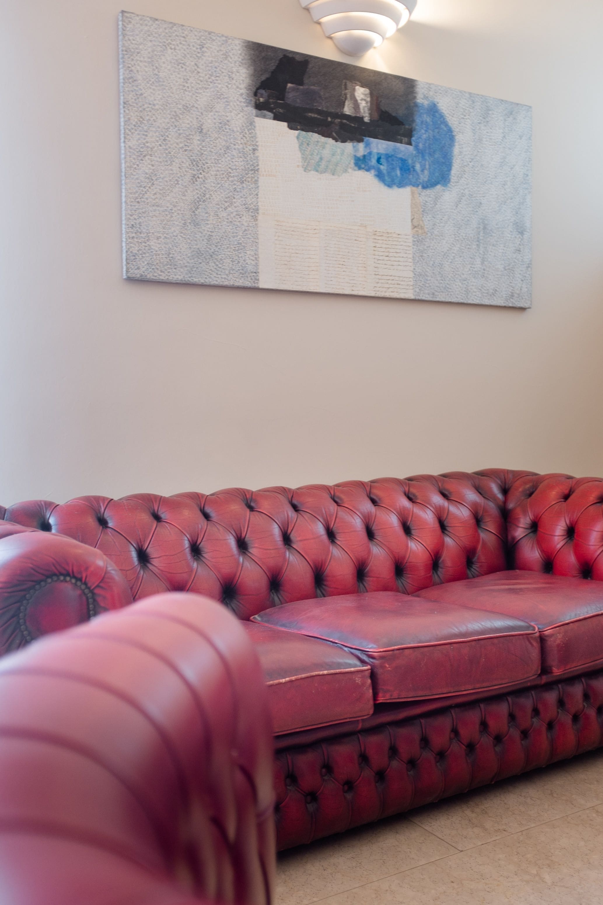 Un sofá de cuero rojo en una habitación con un cuadro abstracto de gran tamaño en la pared.