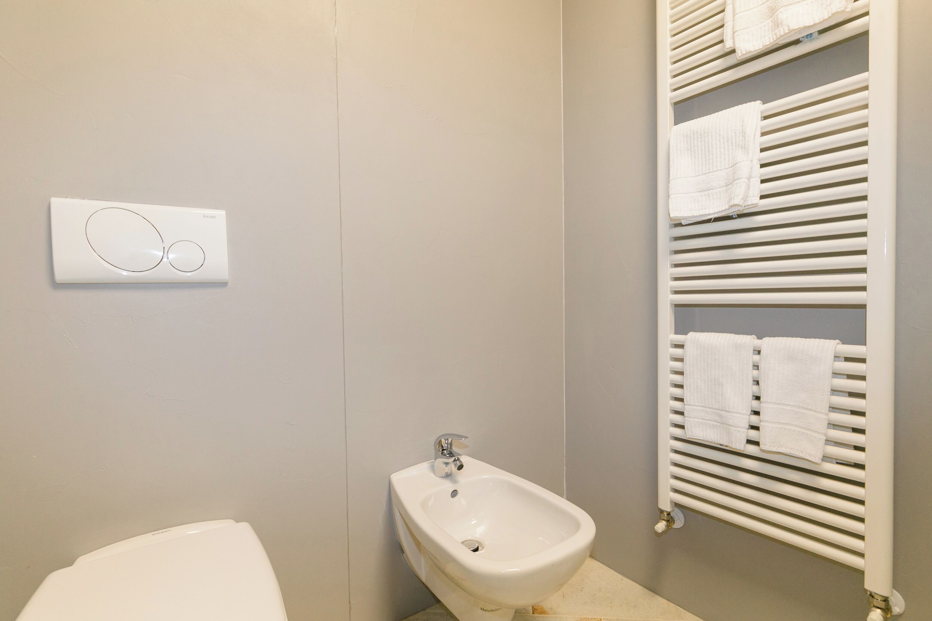 A bathroom with a bidet, a towel rack, and a wall-mounted control panel.
