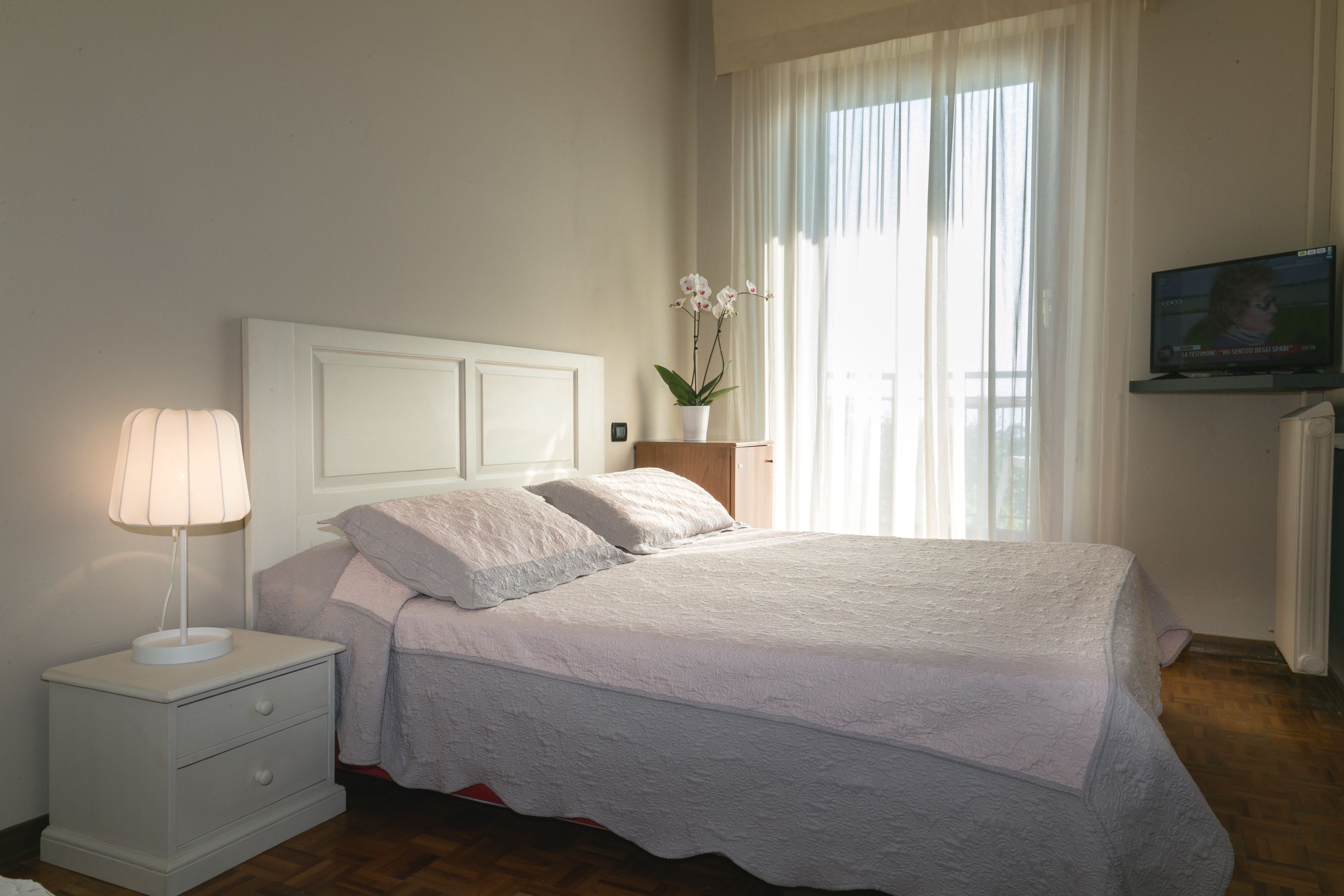 Une chambre à coucher avec un lit, une table de chevet avec une lampe, une plante en pot et un téléviseur fixé au mur.