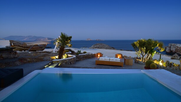 A pool area with a view of the sea, a wooden deck, and a seating area with cushions.