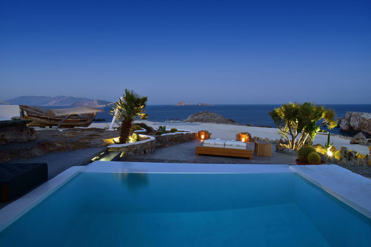 A pool area with a view of the sea, a wooden deck, and a seating area with cushions.