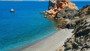 A coastal beach with clear blue waters, rocky cliffs, and a sandy shoreline.