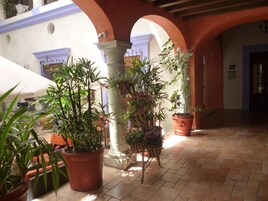 A courtyard with terracotta tiled flooring, potted plants, and a white column.