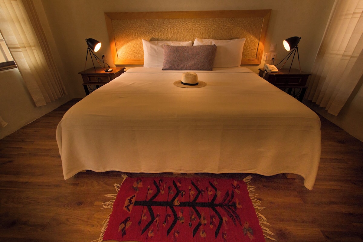 A neatly made bed with a white bedspread, a decorative hat on the bed, and two bedside lamps on wooden nightstands.