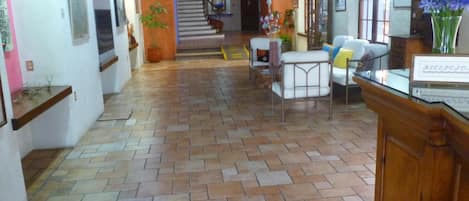 A spacious lobby with a tiled floor, a reception desk, and a staircase leading to upper floors.