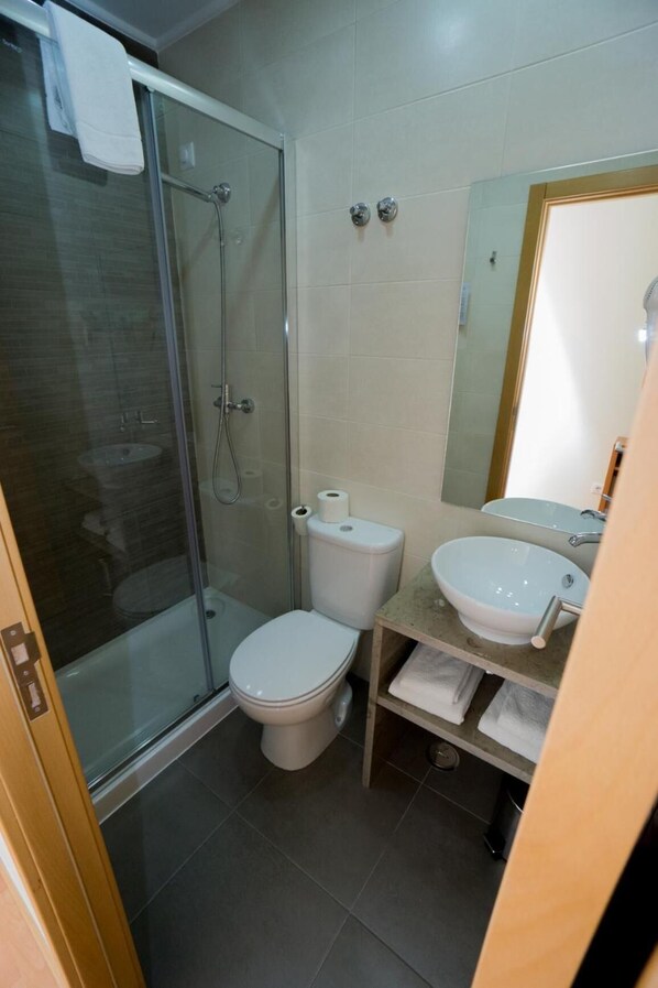 A bathroom with a glass-enclosed shower, a toilet, and a sink with a mirror above it.