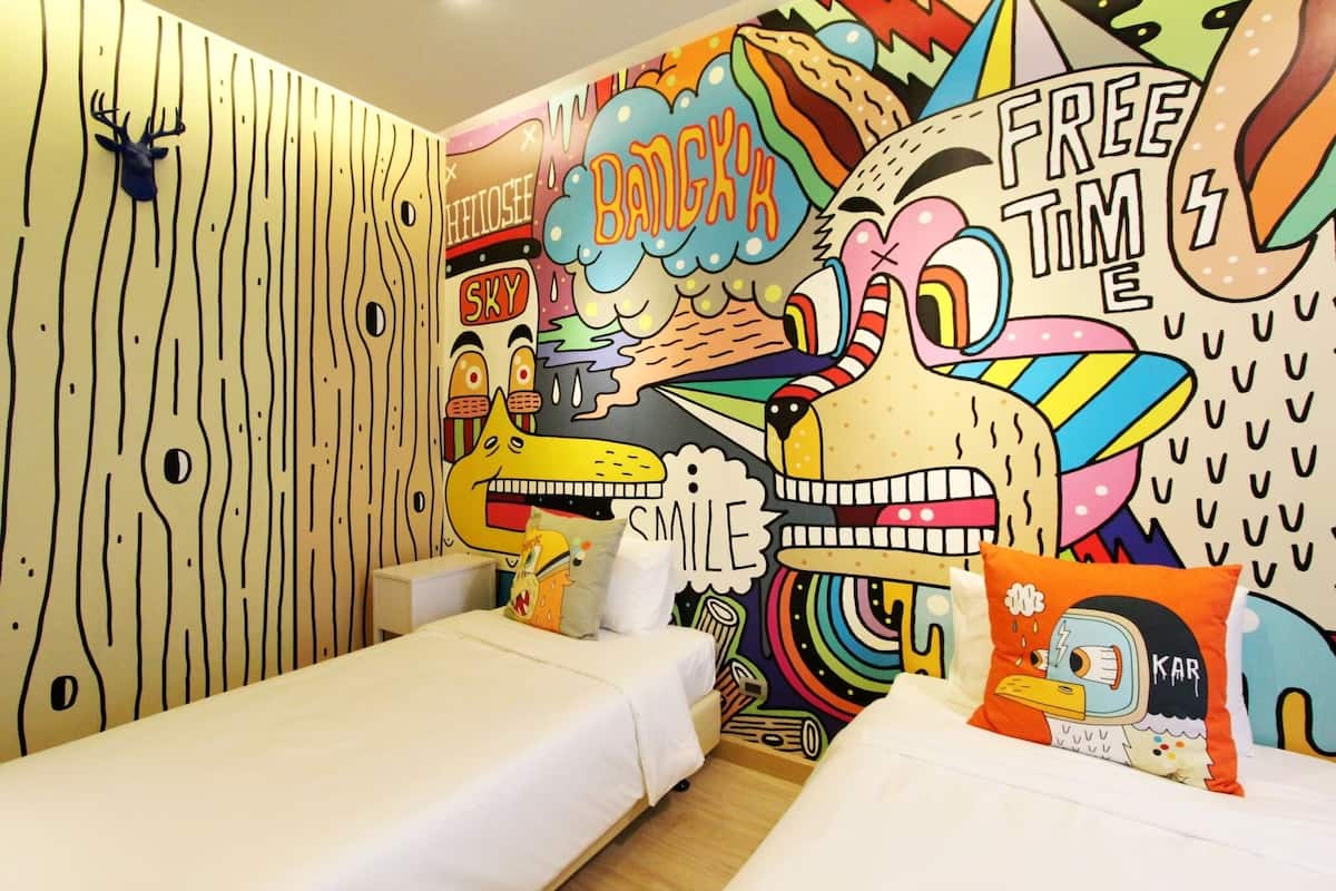 Une pièce agrémentée d’une fresque murale colorée, avec un lit et un petit coin salon.
