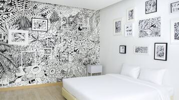 Une chambre à coucher avec un lit blanc, une table de chevet blanche et un mur décoré d’illustrations en noir et blanc encadrées.