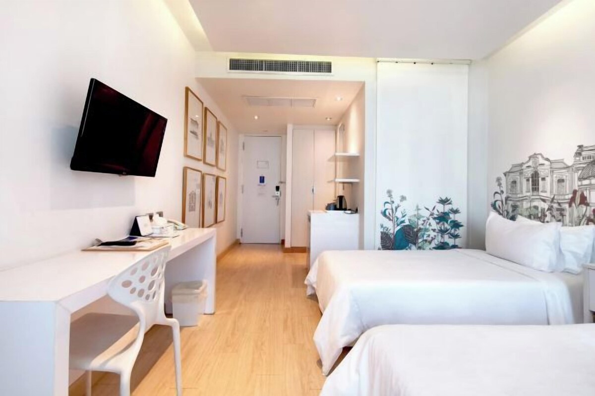 Une chambre d’hôtel équipée d’un bureau, de deux lits, d’une télévision et d’œuvres d’art accrochées aux murs.